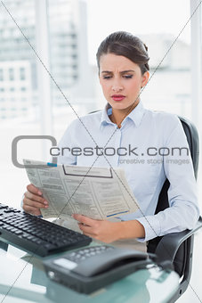 Frowning classy brown haired businesswoman reading a newspaper