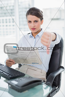 Disappointed classy brown haired businesswoman reading a newspaper
