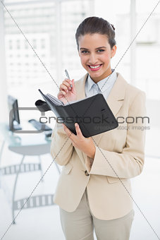 Pleased smart brown haired businesswoman filling an agenda