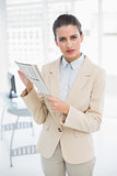 Frowning smart brown haired businesswoman holding a newspaper
