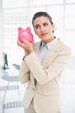 Frowning smart brown haired businesswoman shaking a piggy bank