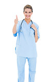 Cheerful brown haired nurse in blue scrubs giving a thumb up