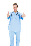 Joyful brown haired nurse in blue scrubs giving thumbs up