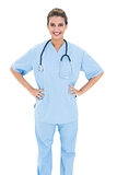 Happy brown haired nurse in blue scrubs posing with hands on the hips