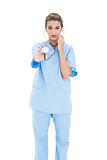 Stern brown haired nurse in blue scrubs using a stethoscope