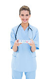 Happy brown haired nurse in blue scrubs holding a medication box