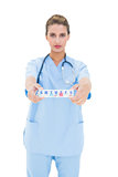 Serious brown haired nurse in blue scrubs showing a medication box