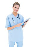 Joyful brown haired nurse in blue scrubs using a tablet pc