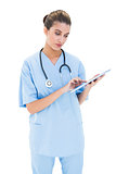 Thoughtful brown haired nurse in blue scrubs using a tablet pc