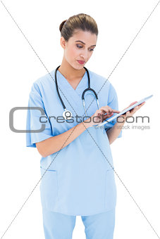 Thoughtful brown haired nurse in blue scrubs using a tablet pc