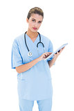 Stern brown haired nurse in blue scrubs using a tablet pc