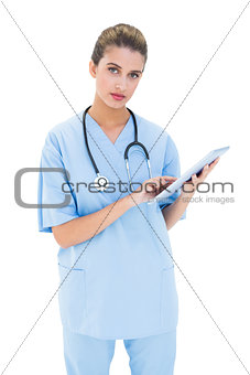 Stern brown haired nurse in blue scrubs using a tablet pc