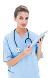 Thinking brown haired nurse in blue scrubs using a tablet pc