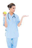 Pretty brown haired nurse in blue scrubs holding a green apple