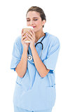 Peaceful brown haired nurse in blue scrubs enjoying coffee smell