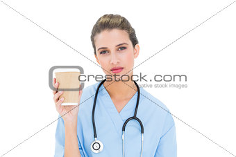 Thoughtful brown haired nurse in blue scrubs holding a cup of coffee