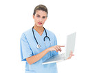 Stern brown haired nurse in blue scrubs using a laptop