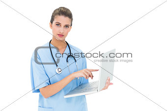 Stern brown haired nurse in blue scrubs using a laptop