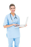 Charming brown haired nurse in blue scrubs using a laptop