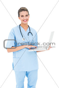 Charming brown haired nurse in blue scrubs using a laptop