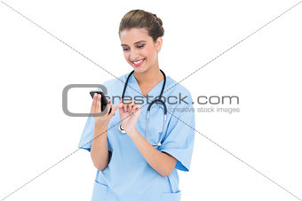 Content brown haired nurse in blue scrubs using a mobile phone