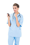Troubled brown haired nurse in blue scrubs using a mobile phone