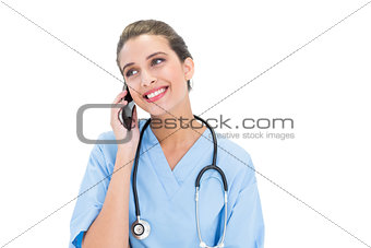 Happy brown haired nurse in blue scrubs making a phone call