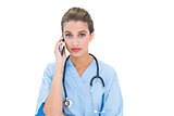 Stern brown haired nurse in blue scrubs making a phone call