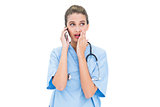 Astonished brown haired nurse in blue scrubs making a phone call