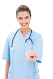 Amused brown haired nurse in blue scrubs offering a pill