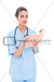 Worried brown haired nurse in blue scrubs reading a book
