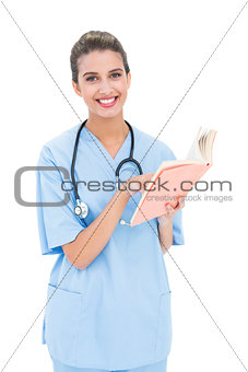 Pleased brown haired nurse in blue scrubs holding a book