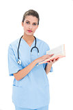 Serious brown haired nurse in blue scrubs holding a book