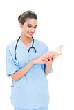 Joyful brown haired nurse in blue scrubs holding a book