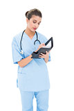 Concentrated brown haired nurse in blue scrubs filling an agenda