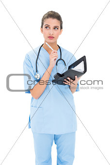 Thoughtful brown haired nurse in blue scrubs holding an agenda