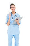 Smiling brown haired nurse in blue scrubs checking a report