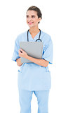 Thoughtful brown haired nurse in blue scrubs holding a clipboard