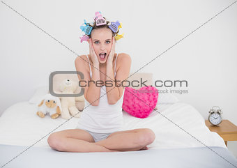 Astonished natural brown haired woman in hair curlers posing looking at camera