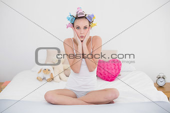 Shocked natural brown haired woman in hair curlers touching her face
