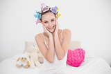 Relaxed natural brown haired woman in hair curlers touching her face