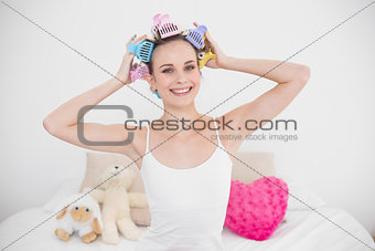 Pleased natural brown haired woman fixing her hair curlers