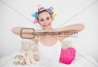 Joyful natural brown haired woman in hair curlers posing looking at camera