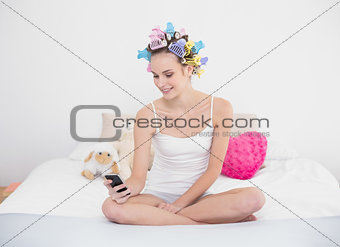 Pleased natural brown haired woman in hair curlers using her mobile phone