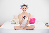 Happy natural brown haired woman in hair curlers using her mobile phone