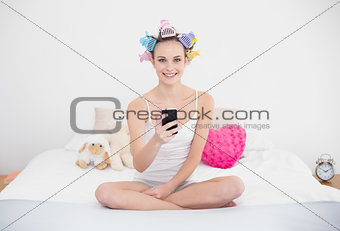 Happy natural brown haired woman in hair curlers using her mobile phone