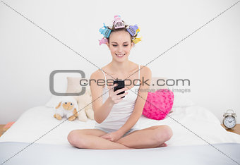 Smiling natural brown haired woman in hair curlers using her mobile phone