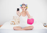Pouting natural brown haired woman in hair curlers taking a picture of herself with mobile phone