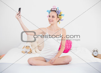 Content natural brown haired woman in hair curlers taking a picture of herself with mobile phone