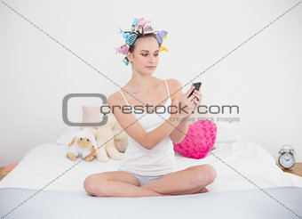 Stern natural brown haired woman in hair curlers using her mobile phone